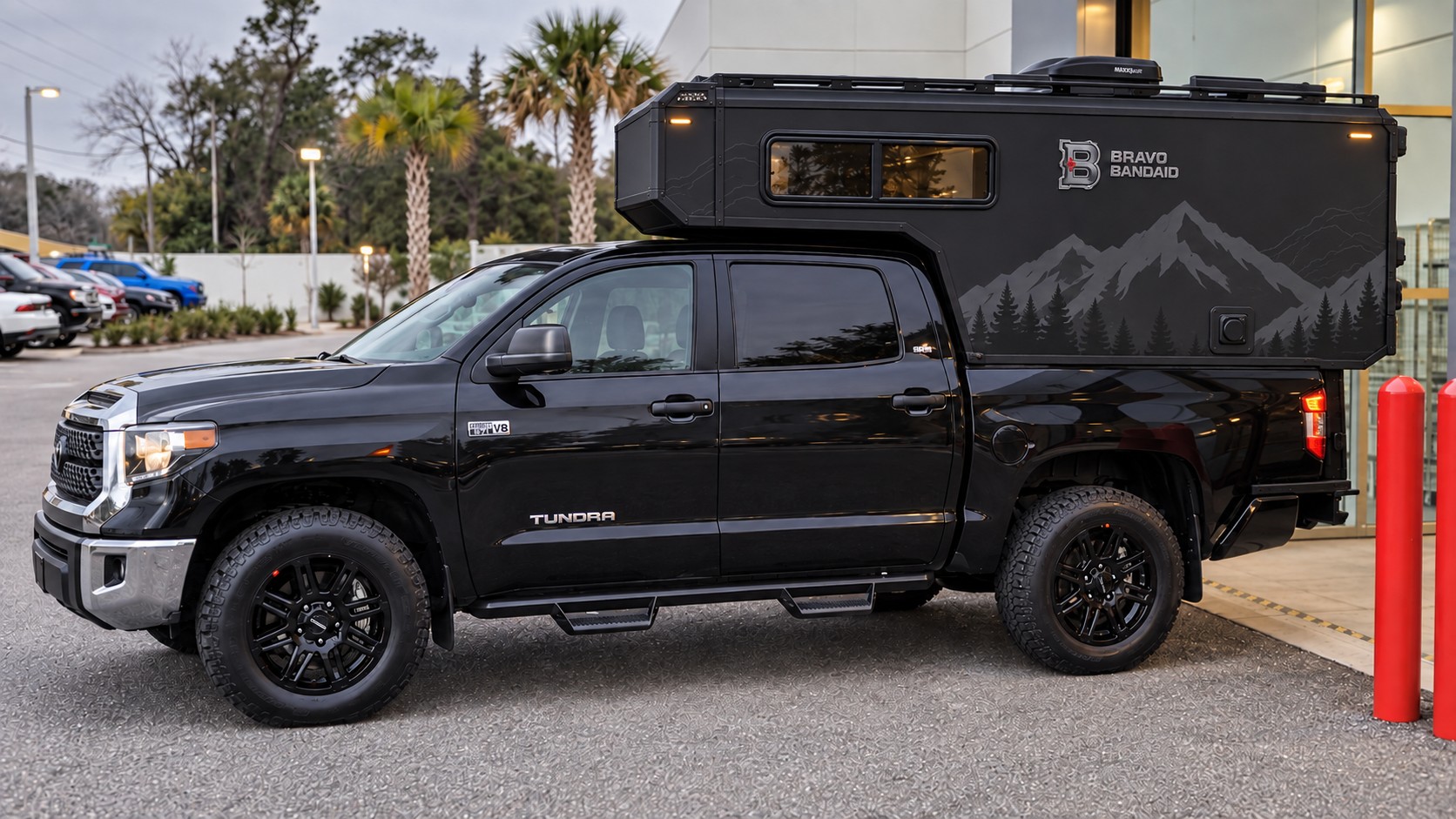 Concept mockup of a black 2021 Toyota Tundra with a dark cab-over camper and mountain graphics.